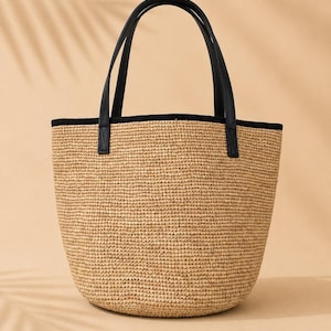 Pu&ograve; includere: Una borsa tote in paglia intrecciata con base arrotondata e una texture in fibra naturale color marrone chiaro. La borsa presenta due manici in similpelle nera fissati al bordo superiore, rifinito con un bordo in tessuto nero solido.