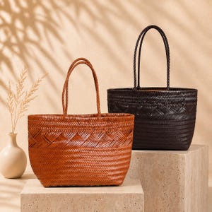 May include: Two woven tote bags with thin handles. One bag is a medium tan color, and the other is a dark brown color. Both bags feature a detailed herringbone weave pattern throughout the body and a horizontal band of decorative woven texture.