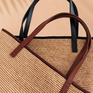 Pu&ograve; includere: Una borsa tote in paglia intrecciata con una texture color marrone chiaro naturale, rifinita con un bordo marrone scuro lungo il bordo superiore e due paia di manici. Una coppia di manici &egrave; nera, l'altra &egrave; marrone scuro, entrambe fissate.