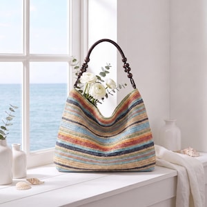 May include: A hobo-style handbag crafted from woven straw featuring horizontal stripes in shades of blue, yellow, orange, and tan. The bag includes a dark brown handle adorned with round wooden beads and contains white flowers with green stems.