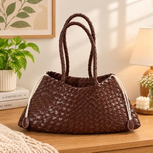 May include: A dark brown woven tote bag featuring a basket-weave pattern, two braided top handles, and white drawstring cords on each side that terminate in small, matching dark brown leather-like tabs at the base of the bag.