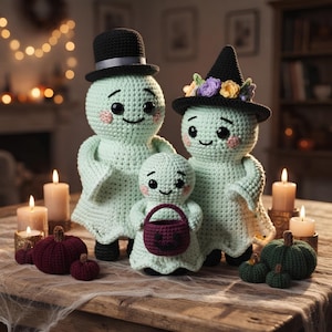 Op de afbeelding: Drie gehaakte spookfiguren van licht muntgroen garen met zwarte knoopogen en roze wangen. De grootste draagt een zwarte hoge hoed, de tweede een zwarte heksenhoed met kleurrijke bloemen en de kleinste houdt een donkerpaars pompoenmandje vast.