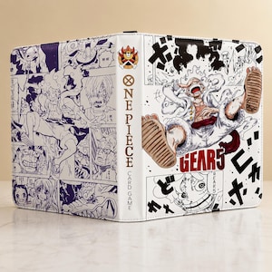 Könnte beinhalten: Ein weißer Sammelkartenordner mit One Piece Gear 5 Grafiken. Der Buchrücken zeigt das One Piece Logo und den Schriftzug. Die Vorder- und Rückseite sind mit schwarz-weißen Manga-Panels bedruckt, während die Vorderseite zusätzlich eine große, farbige Illustration einer Figur in Gear 5 Form sowie den Schriftzug Gear 5 in fetten roten Buchstaben enthält.