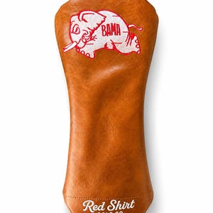 Peut inclure: Un couvre-club de golf en similicuir beige avec un motif brodé d'éléphant blanc aux contours rouges et le texte BAMA en rouge. Le bord inférieur présente le texte brodé en blanc Red Shirt GOLF CO. sur la surface avant de l'objet.