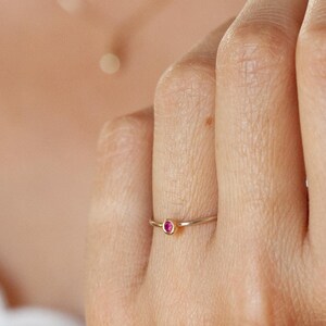 Pode incluir: Um anel de ouro delicado com uma pequena gema vermelha brilhante.