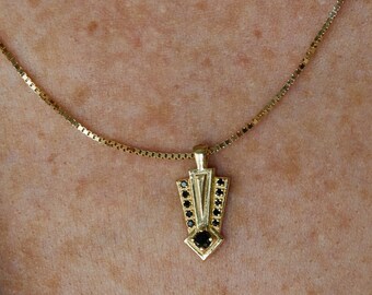 Op de afbeelding: Een gouden ketting met een zwarte diamant hanger in de vorm van een geometrisch ontwerp.
