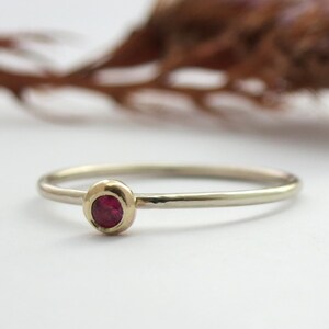 Puede incluir: Un anillo de banda de oro simple con una sola piedra preciosa roja engastada en un engaste de bisel.