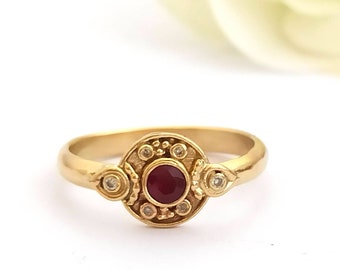 Op de afbeelding: Een gouden ring met een rode edelsteen omringd door kleinere witte edelstenen.