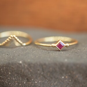 Puede incluir: Dos anillos de oro, uno con una pequeña piedra roja cuadrada y el otro con un diseño decorativo puntiagudo.