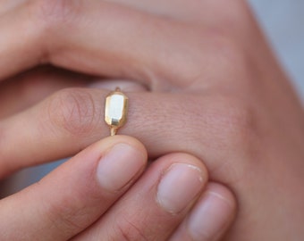 May include: A gold ring with a rectangular, faceted stone. The ring is worn on a finger.