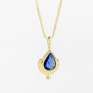 May include: A gold chain necklace with a teardrop-shaped pendant featuring a blue gemstone set in a gold frame.
