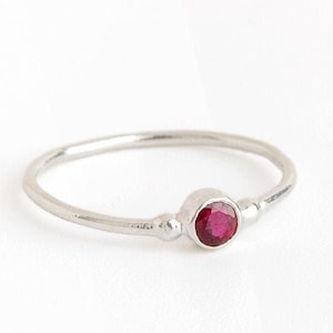 Peut inclure: Une bague en argent simple avec une seule pierre précieuse rouge sertie au centre.