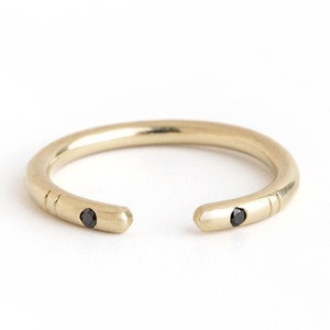 May include: A gold ring with two black diamonds set into the band. The ring is open on one side.