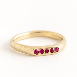 May include: A gold band ring with a row of small red gemstones.