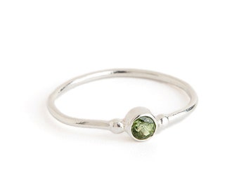 May include: A silver ring with a small, round green gemstone set in the center.