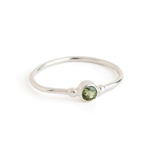 Peut inclure: Une bague en argent avec une petite pierre précieuse ronde verte sertie au centre.