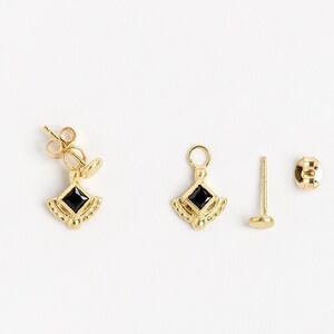 K&ouml;nnte beinhalten: Ein Paar goldene Ohrringe mit schwarzen quadratischen Edelsteinen. Die Ohrringe haben die Form eines kleinen, verzierten, diamantf&ouml;rmigen Anh&auml;ngers. Die Ohrringe werden mit einem Paar goldenen Ohrsteckern geliefert.