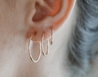 May include: Close-up of an ear adorned with three gold hoop earrings of varying sizes. The earrings are simple and elegant, reflecting light. The person's dark hair is pulled back, and the skin tone is fair.