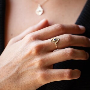 May include: A gold ring with a geometric design featuring a small blue gemstone in the centre.
