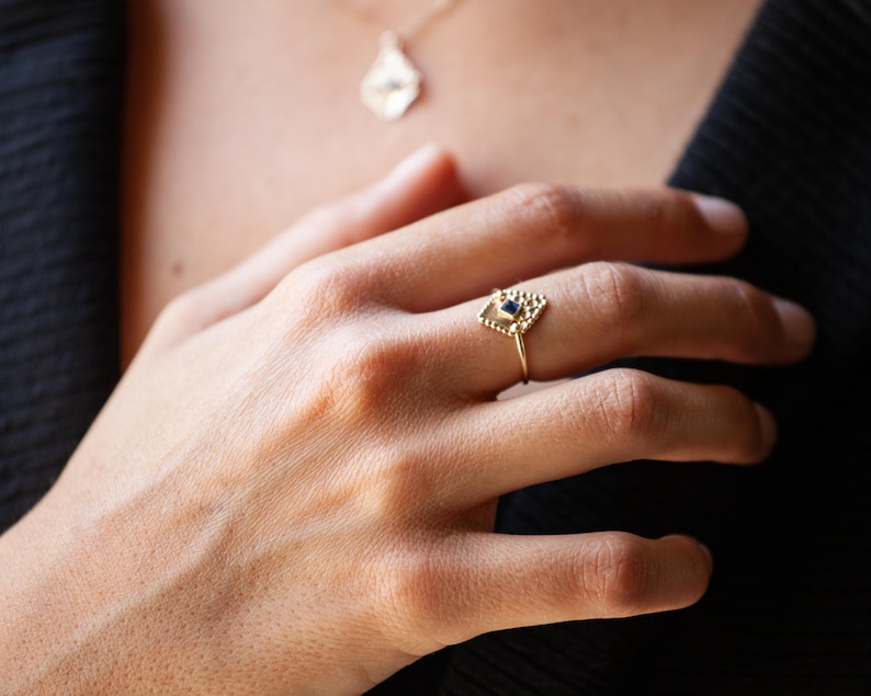 May include: A gold ring with a geometric design featuring a small blue gemstone in the centre.