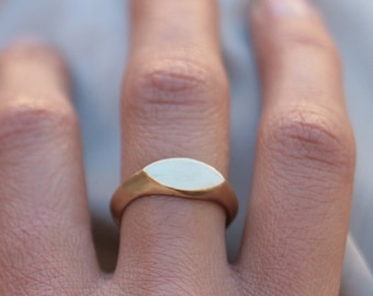 May include: A gold oval signet ring with a smooth, flat top.