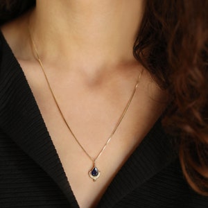 May include: A gold chain necklace with a pendant featuring a blue gemstone surrounded by smaller clear gemstones.