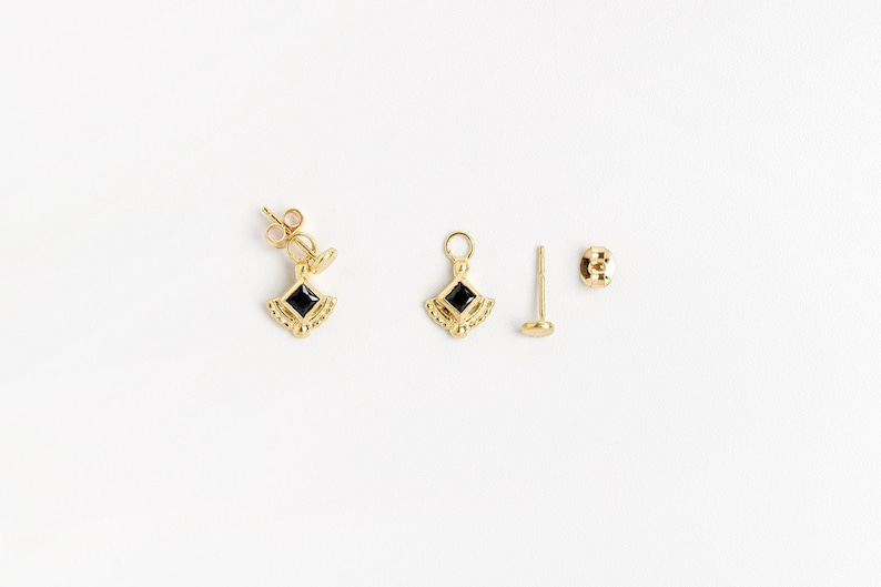K&ouml;nnte beinhalten: Ein Paar goldene Ohrringe mit schwarzen quadratischen Edelsteinen. Die Ohrringe haben die Form eines kleinen, verzierten, diamantf&ouml;rmigen Anh&auml;ngers. Die Ohrringe werden mit einem Paar goldenen Ohrsteckern geliefert.