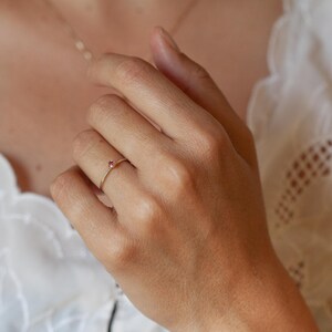 May include: A delicate gold band ring with a small, bright red gemstone set in the centre.