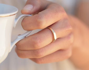 May include: A simple gold band ring worn on a finger.