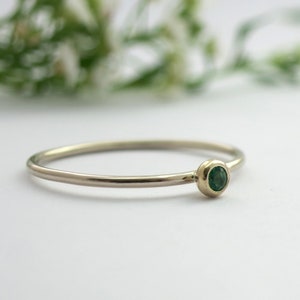 Pode incluir: Um delicado anel de ouro com uma pequena gema redonda de cor verde esmeralda.