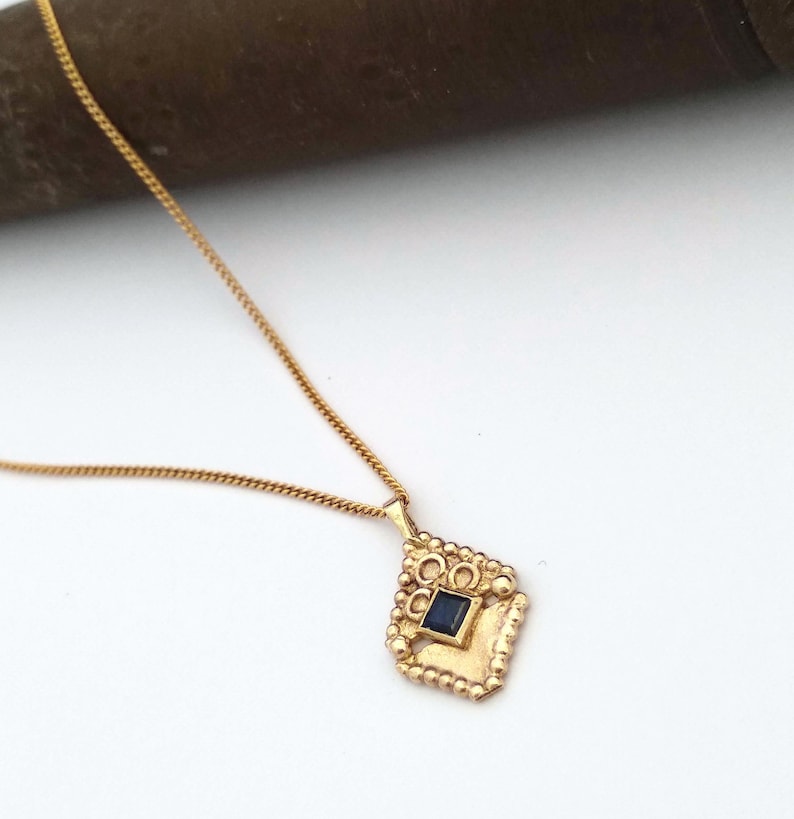 May include: A gold necklace with a pendant featuring a dark blue gemstone set in a gold frame with a decorative design.
