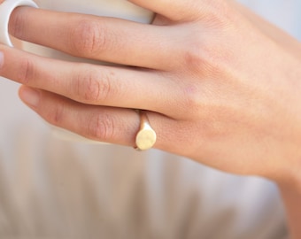 May include: A gold signet ring with a smooth, oval-shaped top.