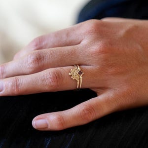 Può includere: Un anello d'oro con una piccola pietra preziosa quadrata di colore viola. L'anello è su un dito.