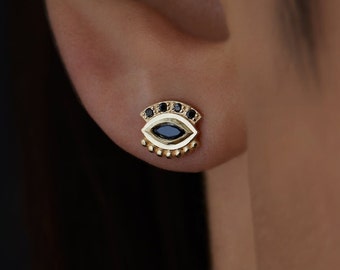 May include: Gold evil eye earrings with black stones. The earrings are small and delicate, and they feature a detailed design.