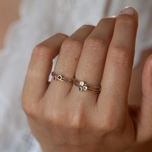 May include: Three gold rings with tiny gemstones. The top ring has a white gemstone, the middle ring has a blue gemstone, and the bottom ring has a red gemstone.