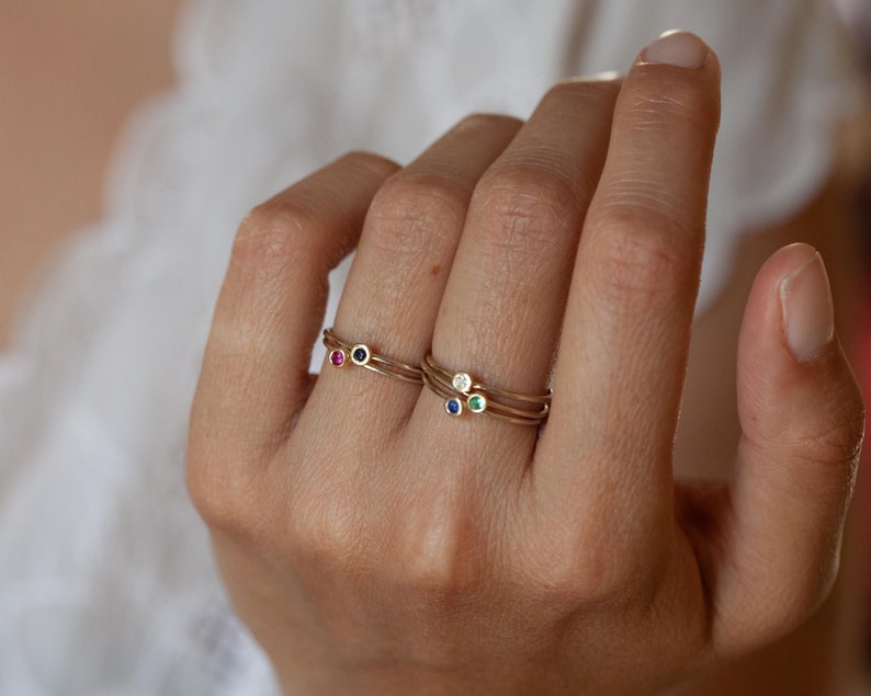 May include: Three gold rings with tiny gemstones. The top ring has a white gemstone, the middle ring has a blue gemstone, and the bottom ring has a red gemstone.