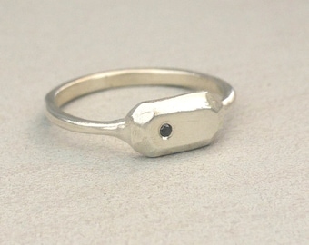 May include: A silver ring with a rectangular, faceted band and a small black gemstone set in the centre.