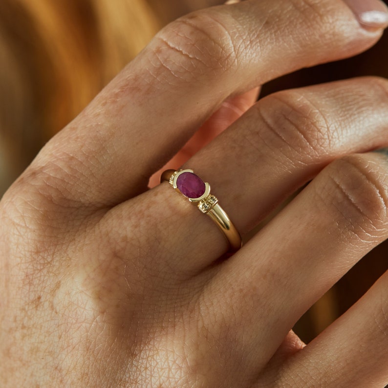 K&ouml;nnte beinhalten: Ein goldener Ring mit einem roten ovalen Edelstein und kleinen goldenen Akzenten.