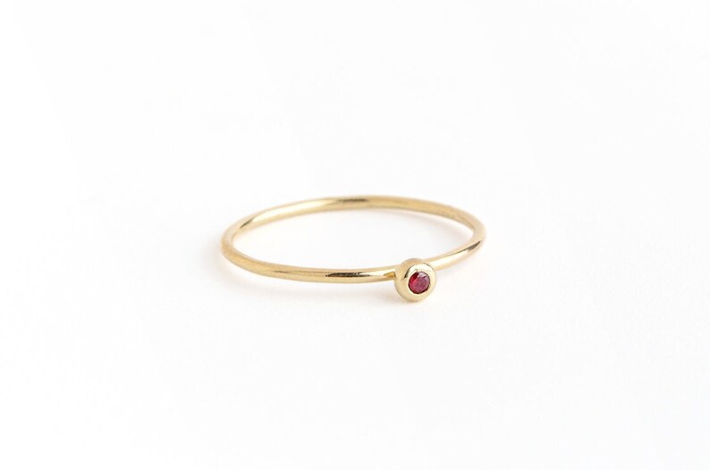 May include: A simple gold band ring with a small red gemstone.