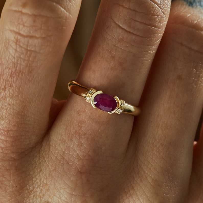K&ouml;nnte beinhalten: Ein goldener Ring mit einem roten ovalen Edelstein und kleinen Diamanten auf der Ringschiene.