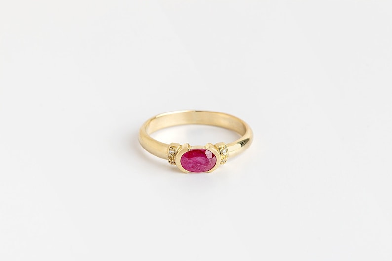 K&ouml;nnte beinhalten: Ein goldener Ring mit einem roten ovalen Edelstein und kleinen Diamanten auf der Ringschiene.