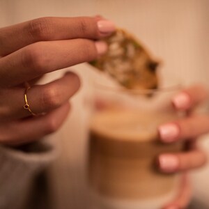 May include: A gold ring with a small red gemstone. The ring is on a person's finger.