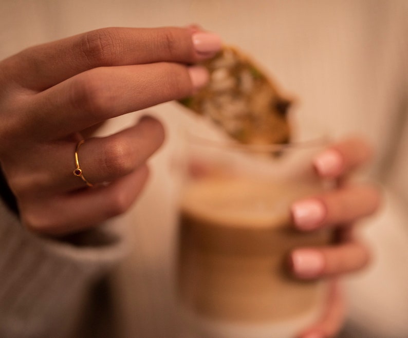 May include: A gold ring with a small red gemstone. The ring is on a person's finger.