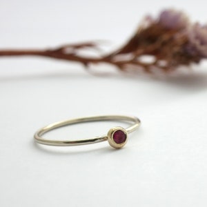 May include: A delicate silver ring with a small, round, red gemstone set in a gold bezel.