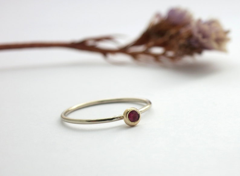 May include: A delicate silver ring with a small, round, red gemstone set in a gold bezel.