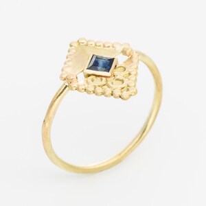 May include: A gold ring with a delicate, ornate design featuring a small, square blue sapphire gemstone.