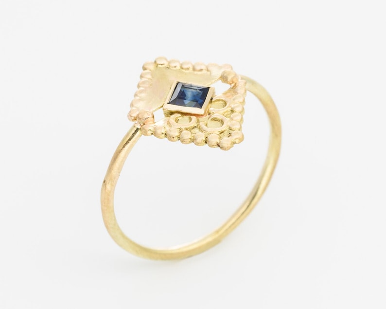 May include: A gold ring with a delicate, ornate design featuring a small, square blue sapphire gemstone.