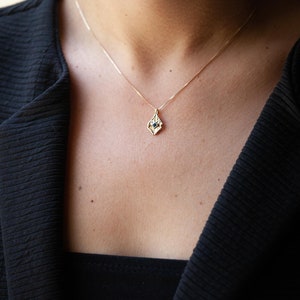 May include: A gold necklace with a delicate pendant featuring a small blue gemstone set in a geometric design.