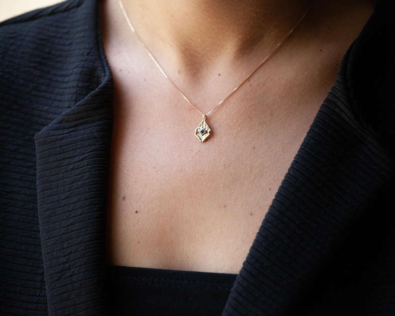 May include: A gold necklace with a delicate pendant featuring a small blue gemstone set in a geometric design.