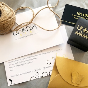 May include: A white card with the text "UNKIYA jewellery workshop" and a message about a 10% discount on the next purchase. A black box with the text "UNKINA jewellery workshop" and a gold envelope with a butterfly design.